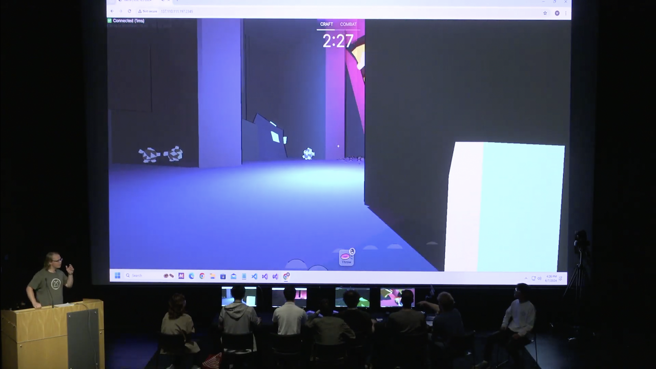 Gameplay being projected onto large auditorium screen while players sit at computers onstage with their backs to the audience